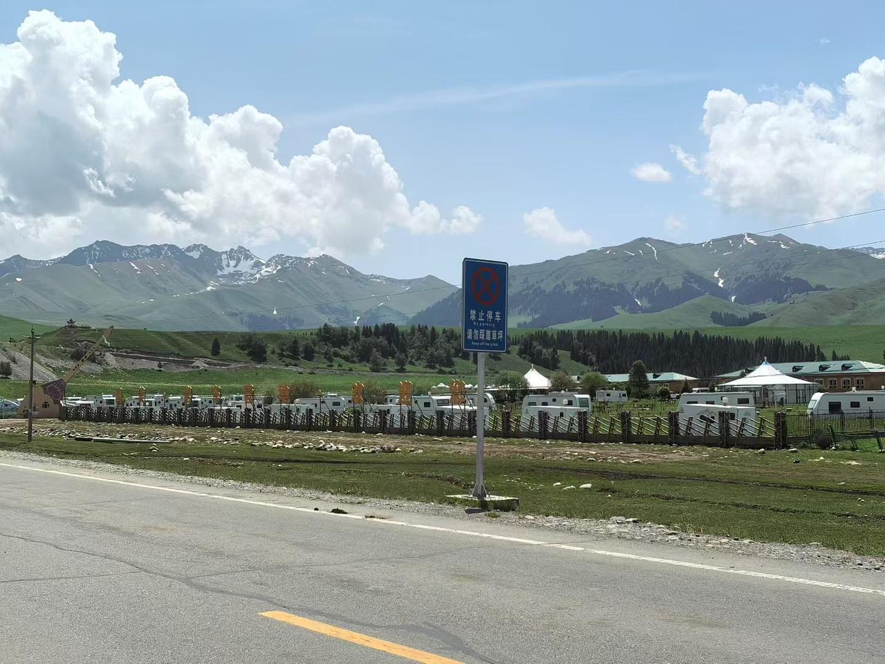 旅行随手拍连绵青山覆着浅浅积雪，大朵白云悬在澄澈蓝天之下，路边草地围起房车营地，
