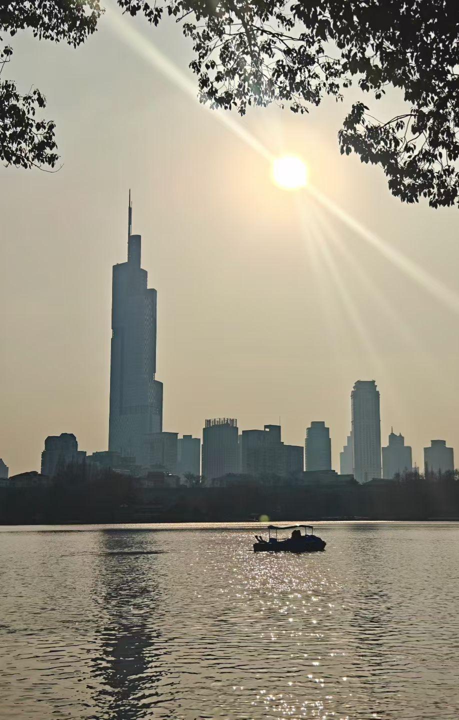 太阳把金箔撒向湖面，游船载着碎光游弋，远处楼宇在薄雾里站成城市的诗，每一道轮廓都