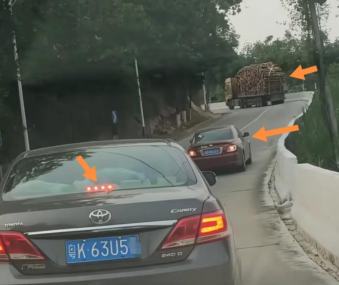 两辆黑色轿车上山停车等待前货车上坡和转弯。