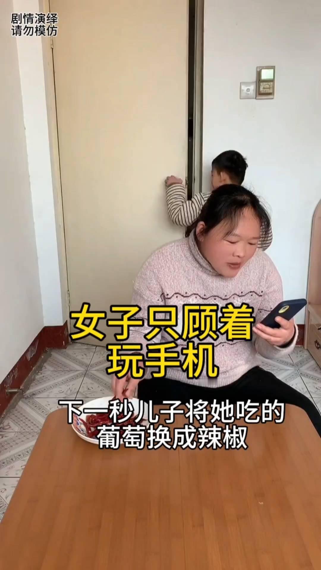 女子只顾着玩手机，下一秒儿子将她吃的葡萄换成辣椒。
女子玩着手机吃着葡萄，这时儿