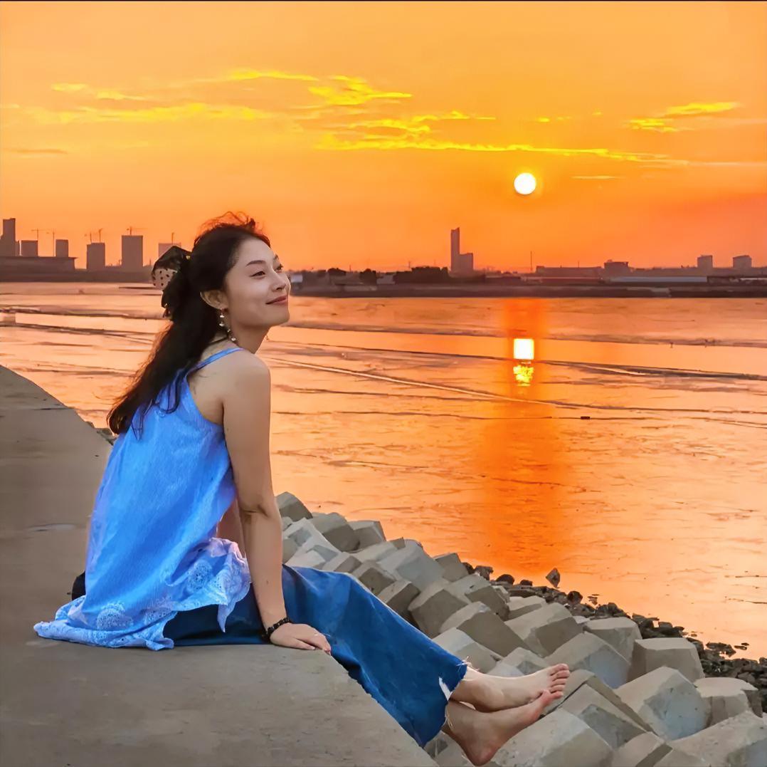 手机抓拍落日夕阳美景，夕阳西下，美女扰闲的座在海边，海风吹过，看到这美景，拿起手