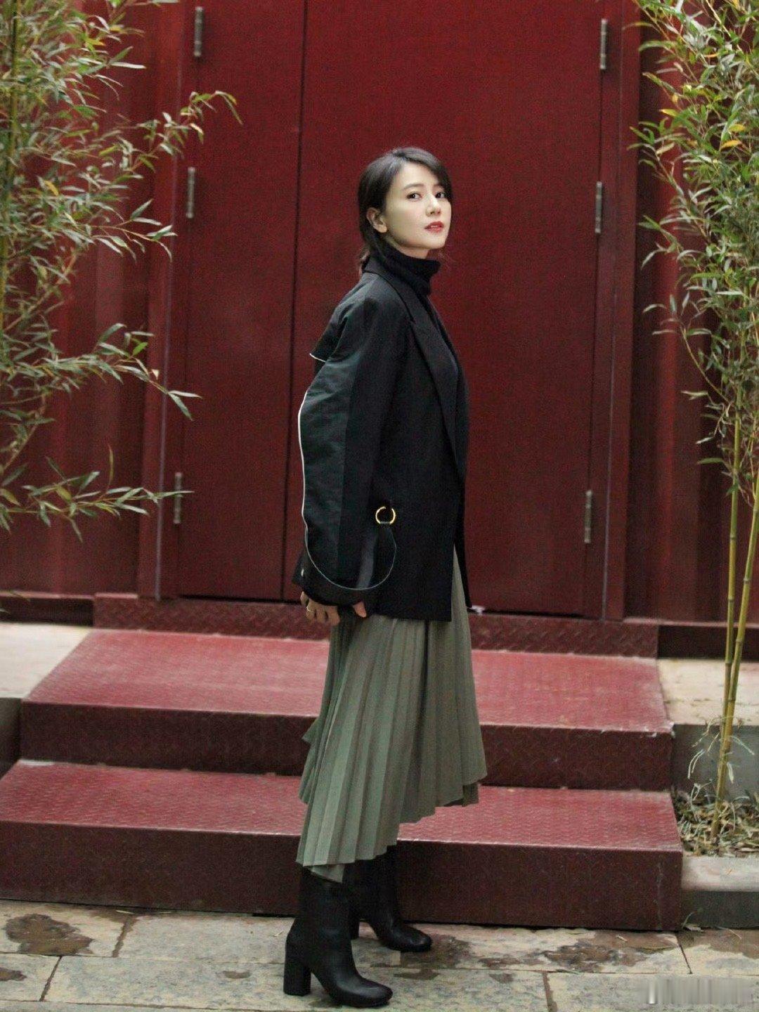 一身穿搭简约又高级，黑色西装搭灰绿百褶裙，红门竹景衬得优雅大气。 