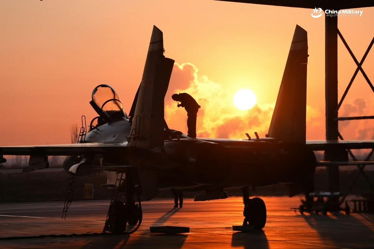 晨曦撕破天际，熔金般的霞光将歼-11的机身勾勒出硬朗的轮廓，机务人员的身影在战机