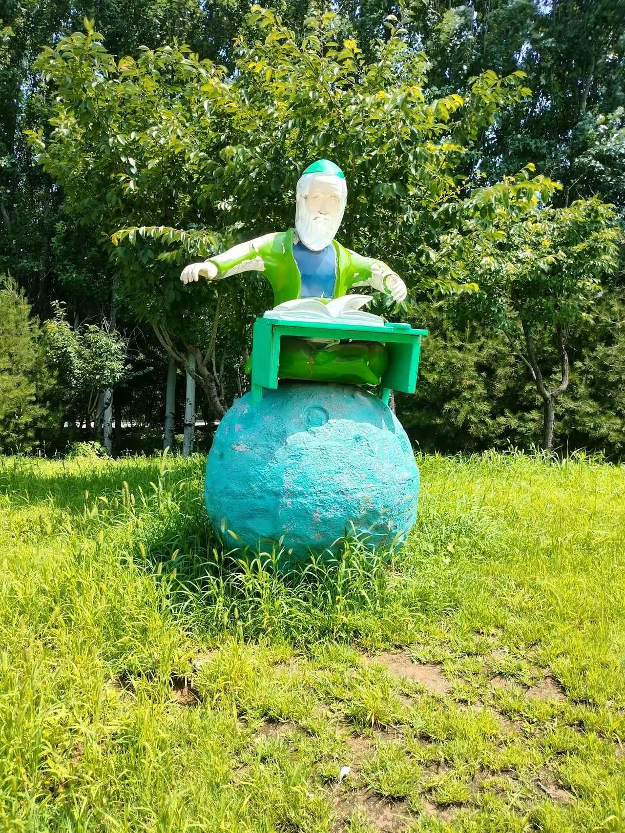 我和老公漫步樱花公园，撞见独坐星球读书的老者雕塑。
在绿地密林之间，彩色雕塑自成