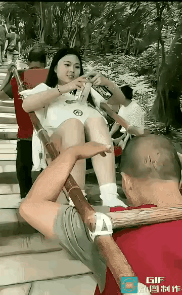 2名登山工大爷抬着一名年轻女子爬泰山，女子躺在担轿上悠闲自得刷着手机，登山工大业