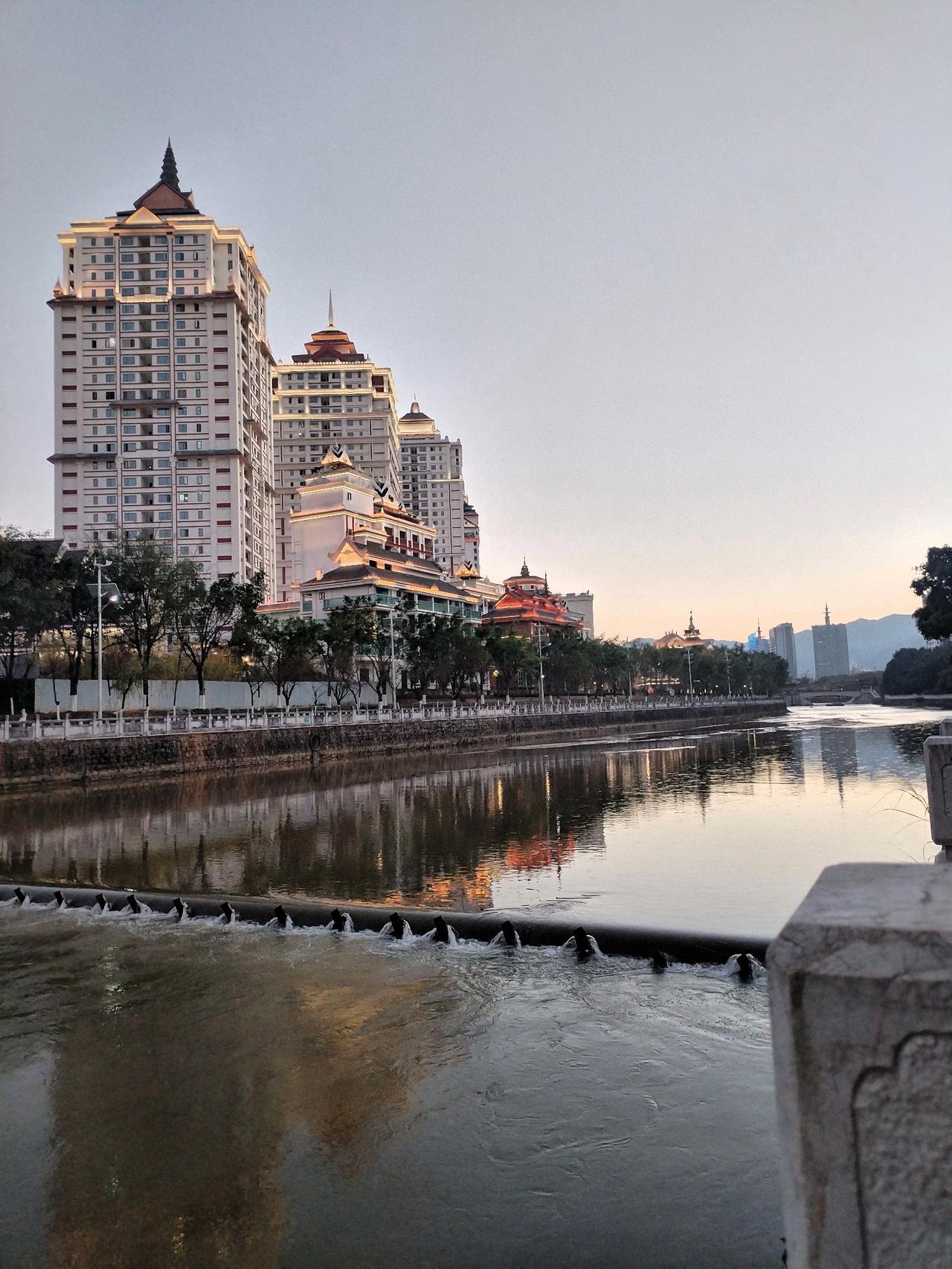 黄昏时分，城市河畔的宁静与繁华交织，倒映在水中的灯光与建筑相映成趣。