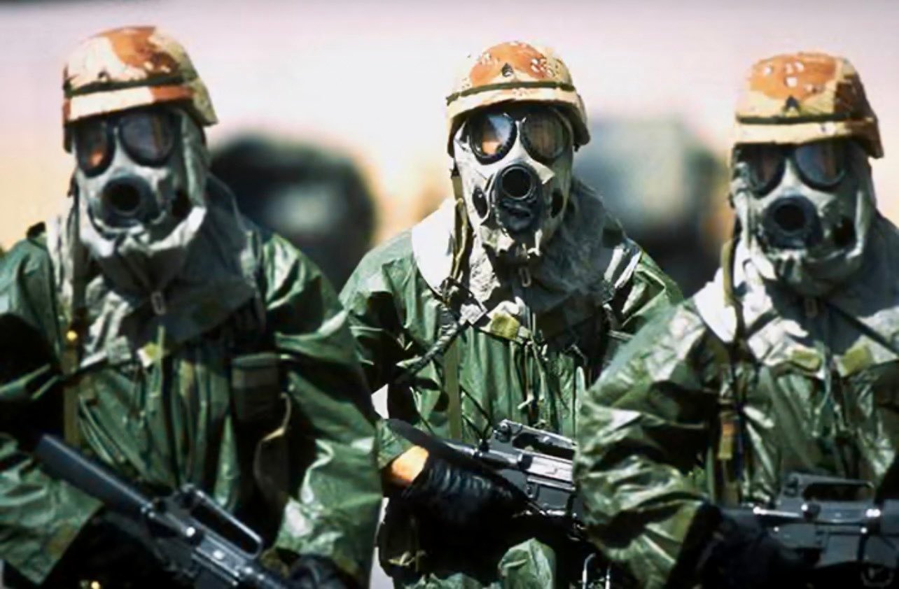 1991年4月，美军82空降师的三名士兵戴着防毒面具和雨具四处走动，以适应沙特夏