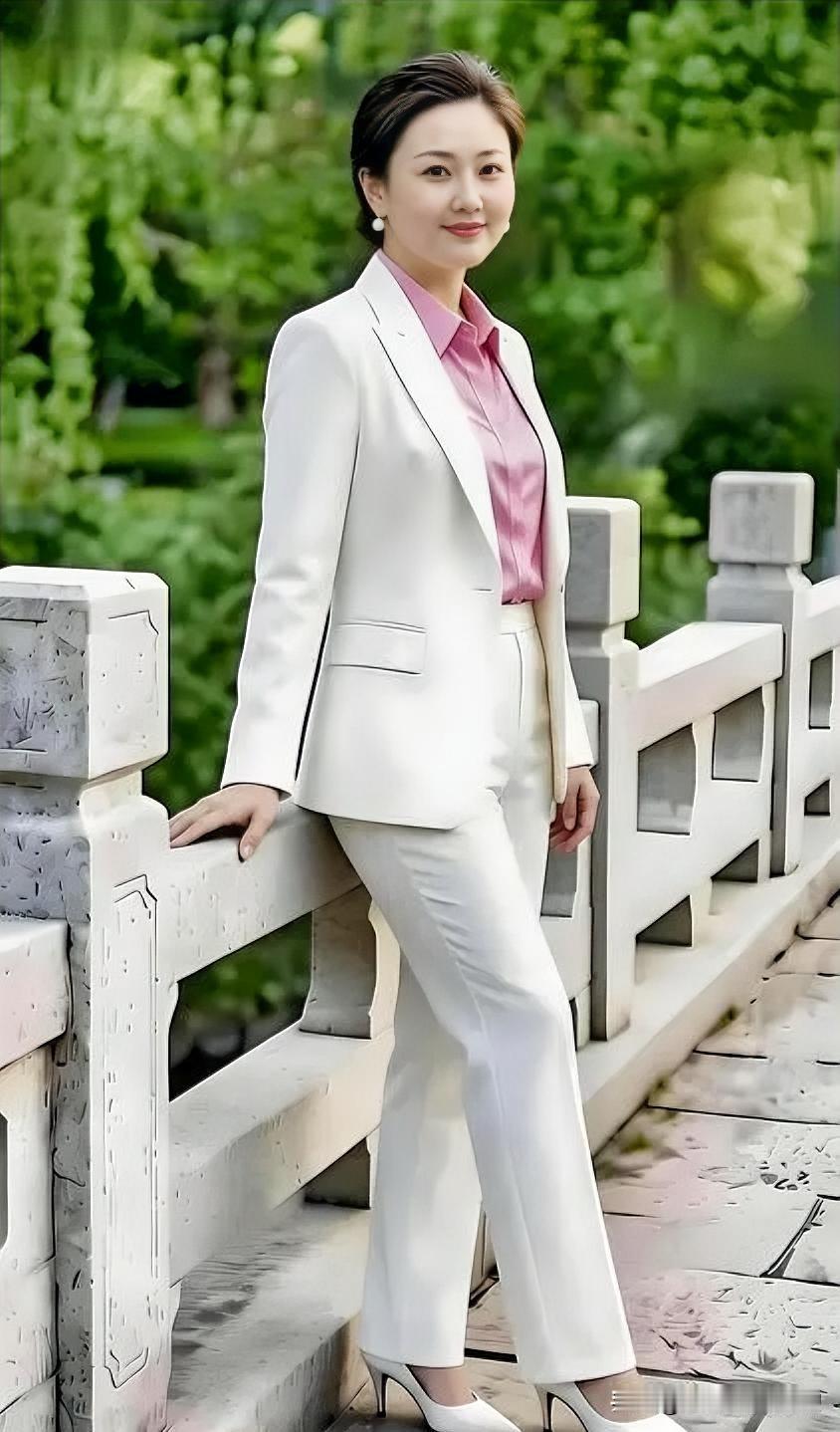 白西装映粉衬衫，倚桥栏而立，干练与温婉在自然绿意中完美交融。