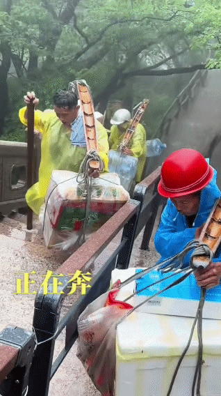 大雨中的黄山，山道湿滑难行，几位挑山工大叔正扛着沉重的货物，沿着陡峭的石阶一步步