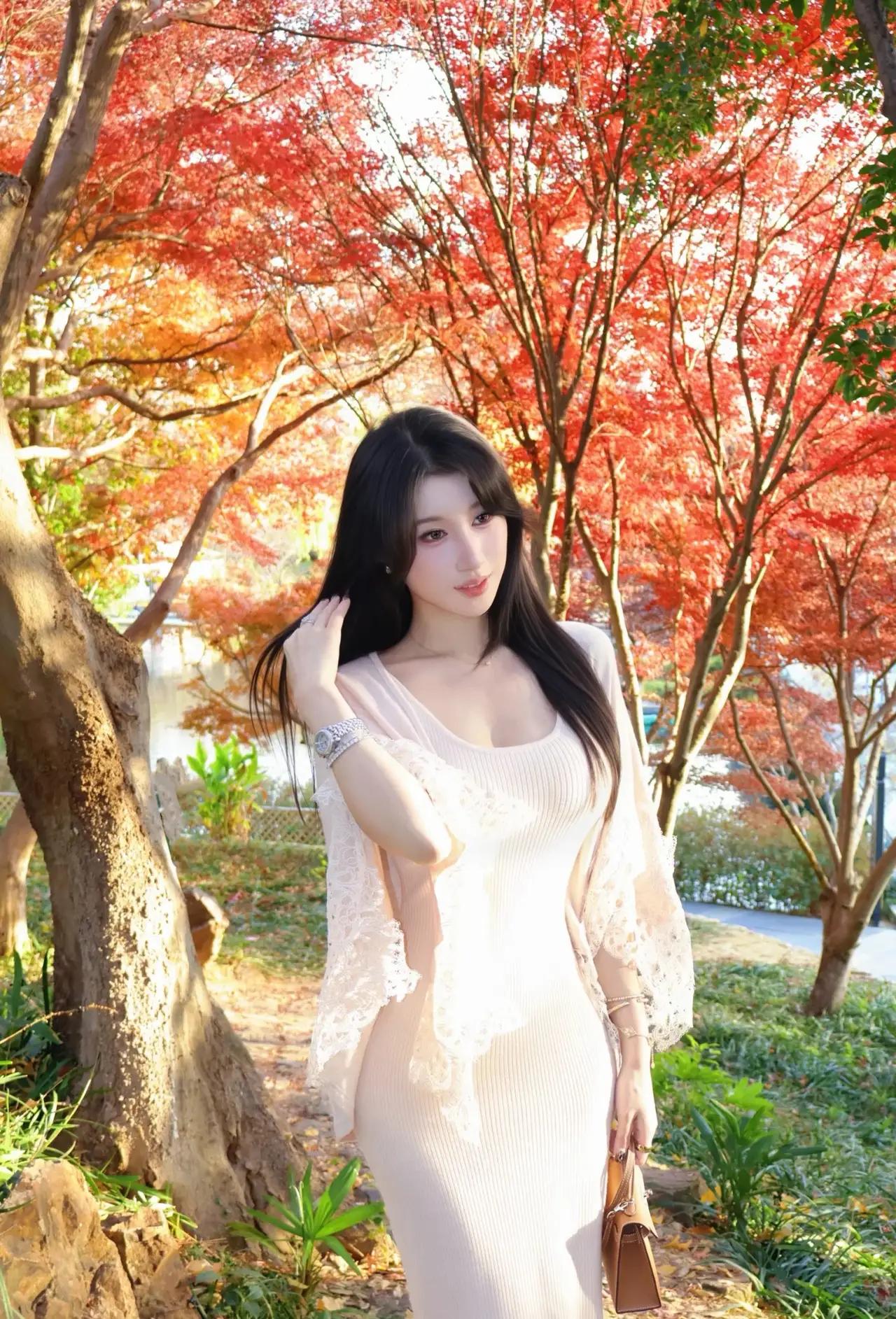 秋日的午后，阳光透过层层叠叠的红叶，洒在一位优雅女性的身上。她站在一片秋意盎然的