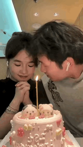 餐厅内男朋友为女友生日庆生，桌上准备好一个漂亮蛋糕，点起了许愿的蜡烛，女友双手合