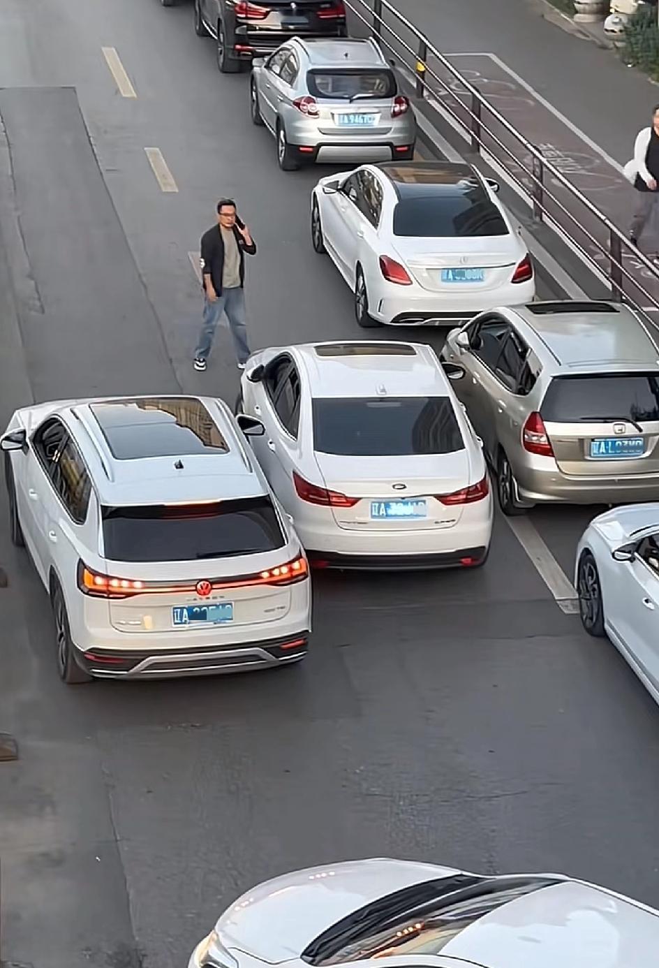 沈阳，一位戴眼镜的男子直接将车停在了马路中间，这条街原本两条道，加上路边已经停了