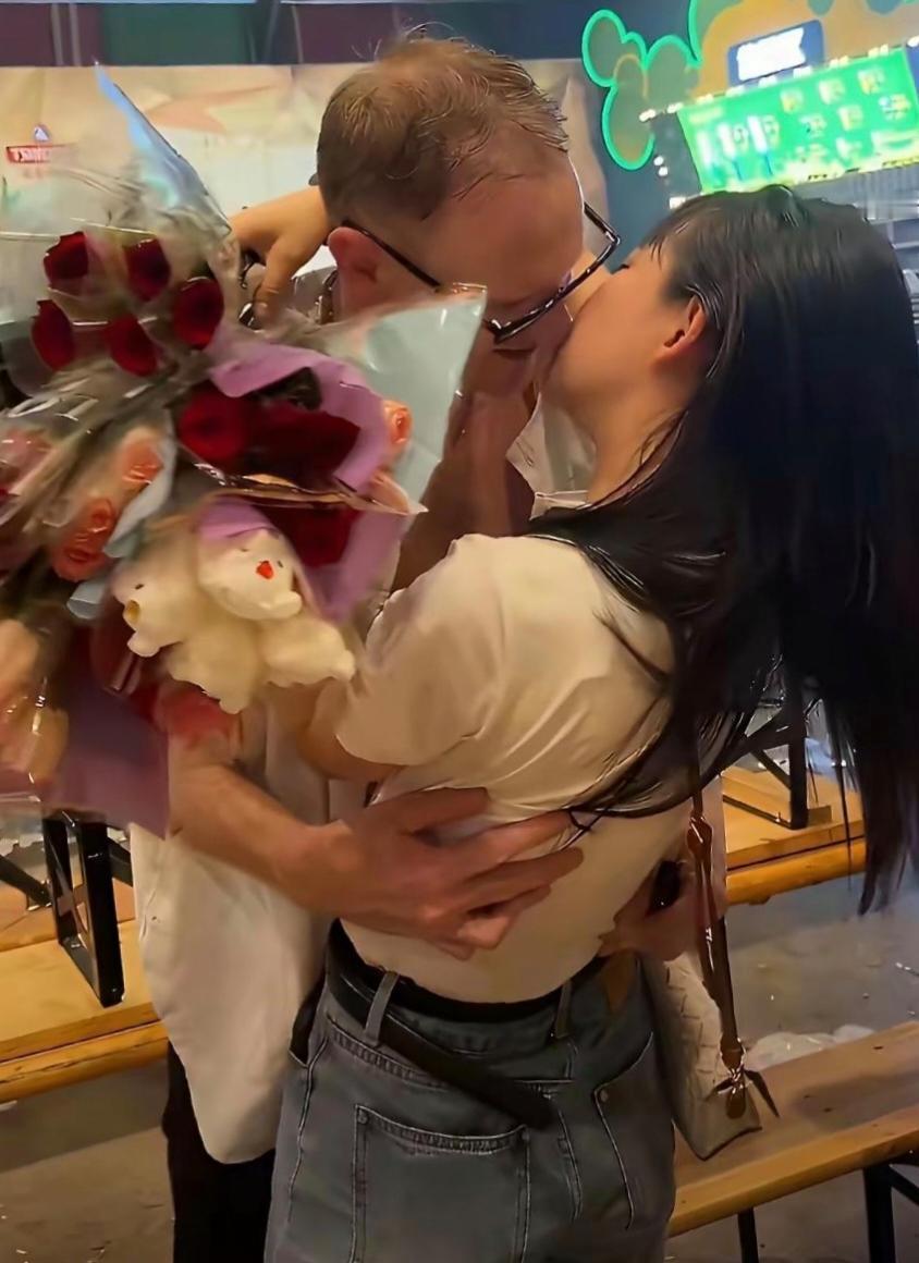 女生拿着一束红玫瑰，主动上前拥抱亲吻对方，当众释放爱意甜度爆表。 