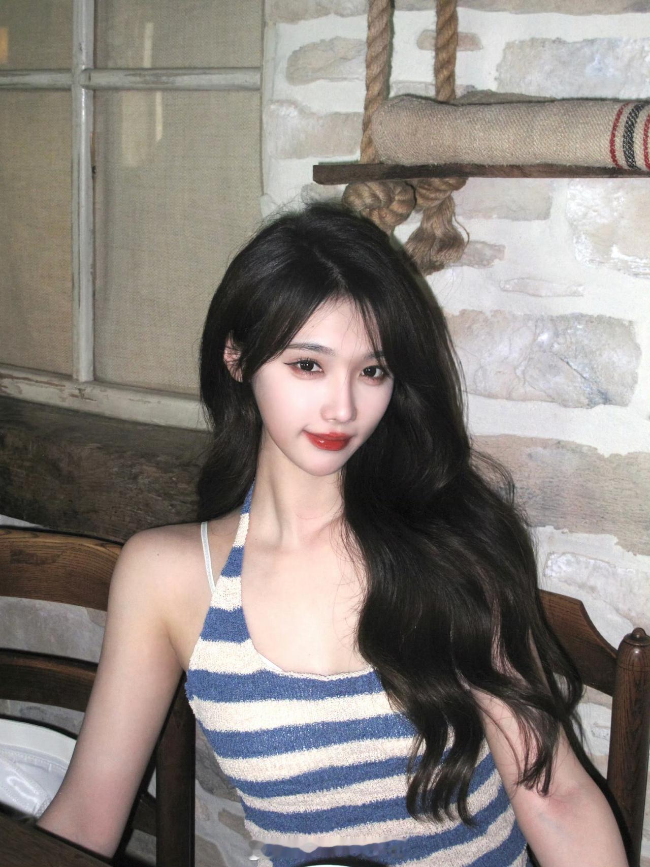 这个女生坐在木椅上，穿着条纹背心。