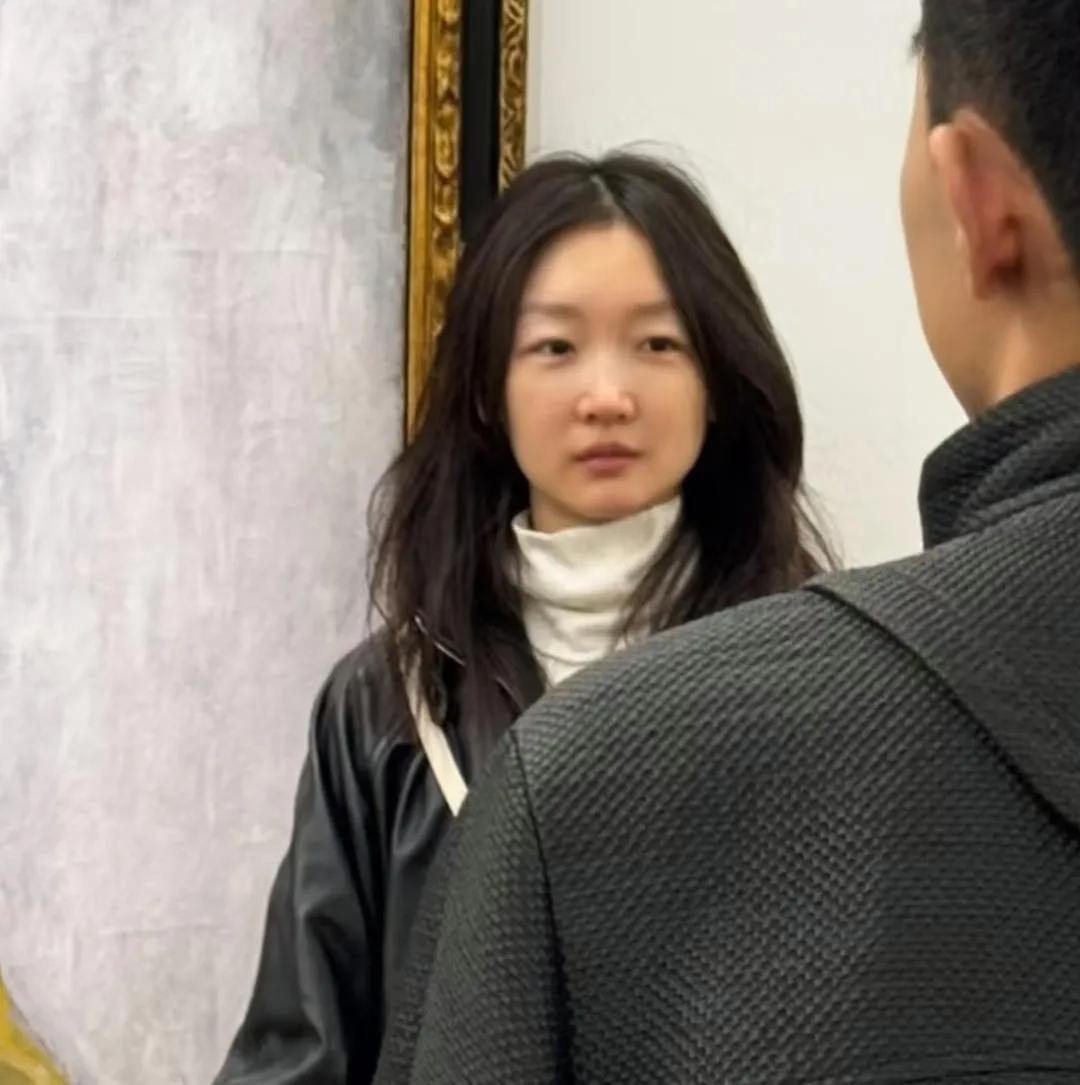 周冬雨现身法国巴黎逛艺术馆，她穿着黑皮夹克，白高领毛衣，头发随意散着，整个人散发