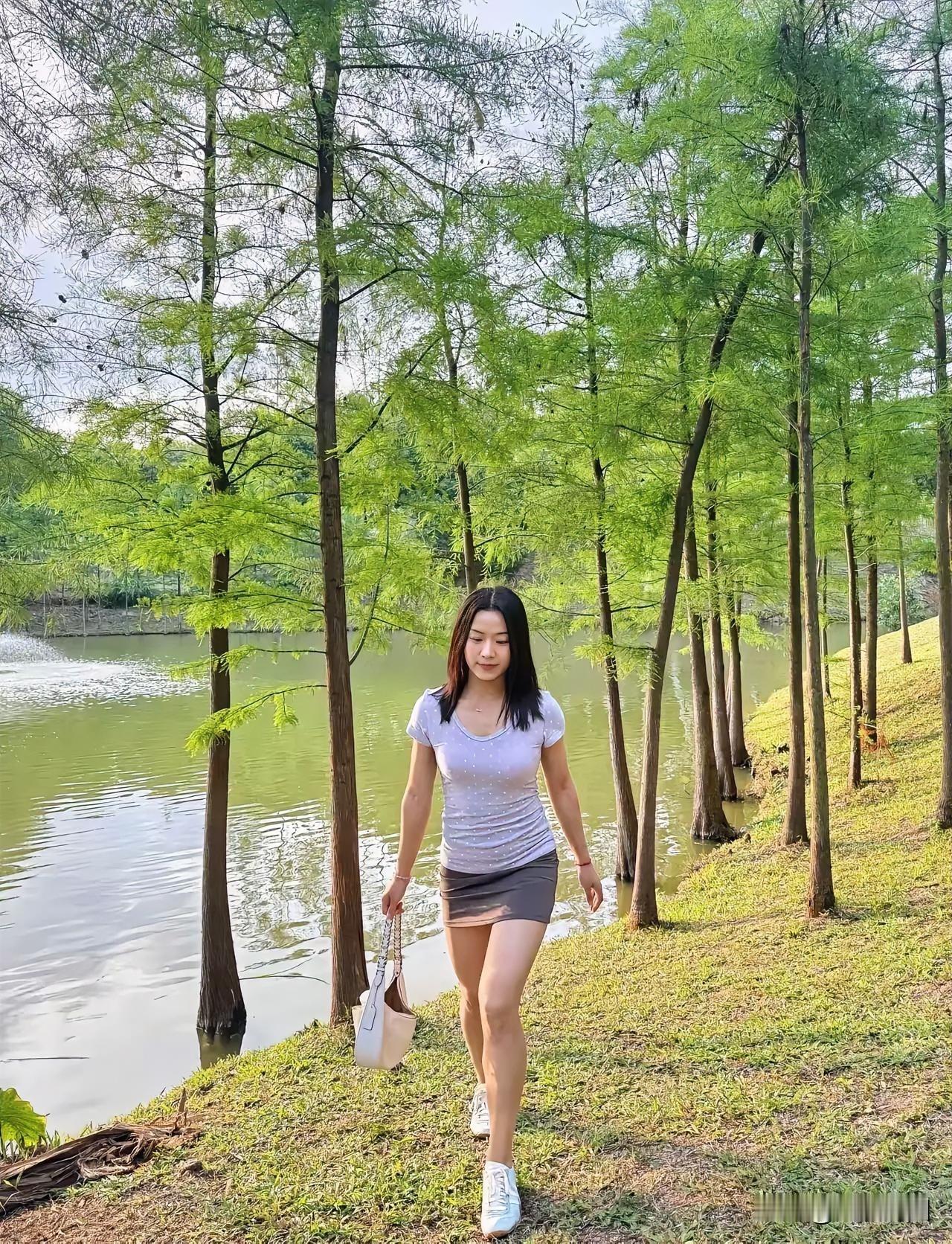 在河边的树林里，美女如同灵动的精灵。阳光透过树叶的缝隙洒下，形成一片片光影，映在