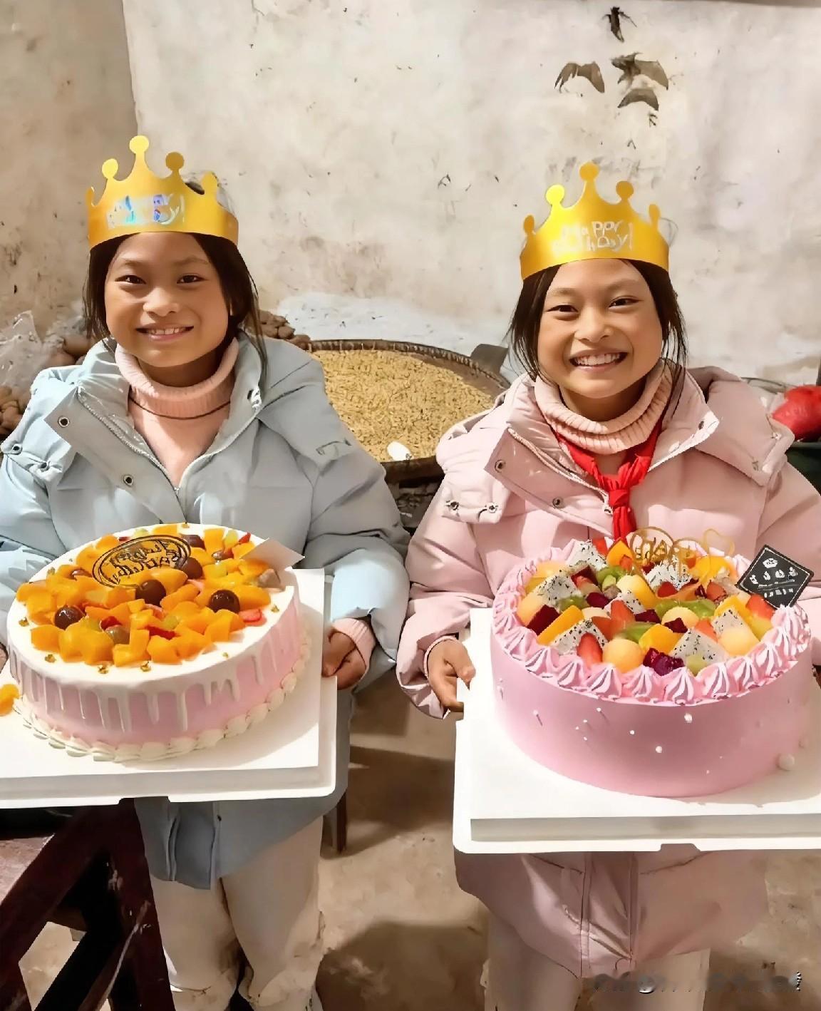 一对双胞胎姐妹一人端着一个生日 蛋糕站在桌子旁，虽然房屋看着非常简陋，但她们满面