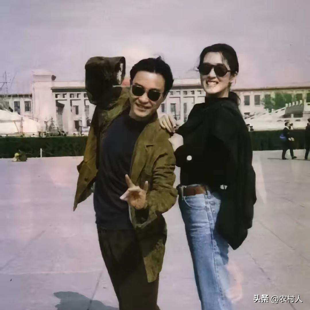 张国荣身穿棕黄色休闲外套，深色内搭，俏皮比出手势。巩俐一身黑色上衣搭配复古直筒牛