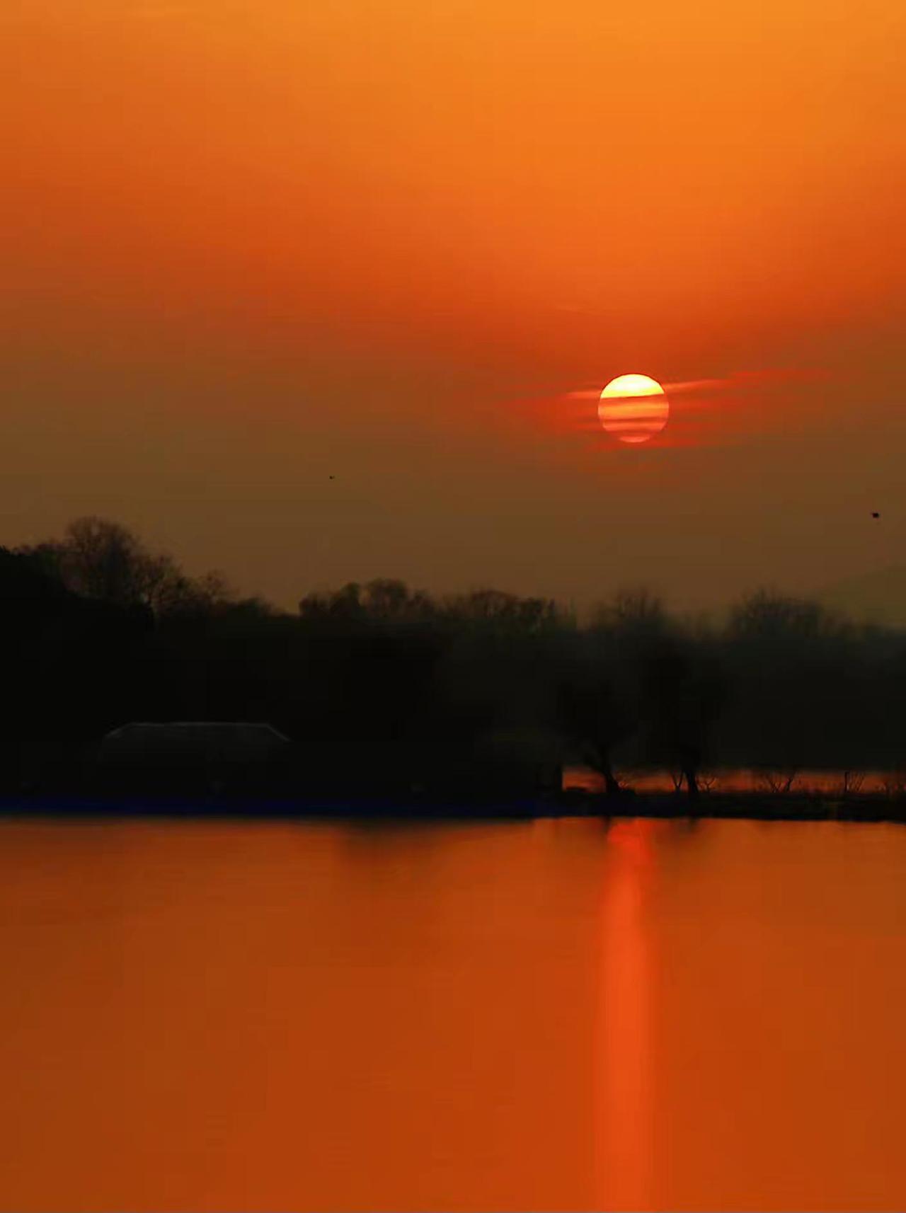 夕阳下的洞庭湖湖夕阳缓缓沉入湖面，天空被染成温柔的橘红色。湖面如镜，倒映出整个世