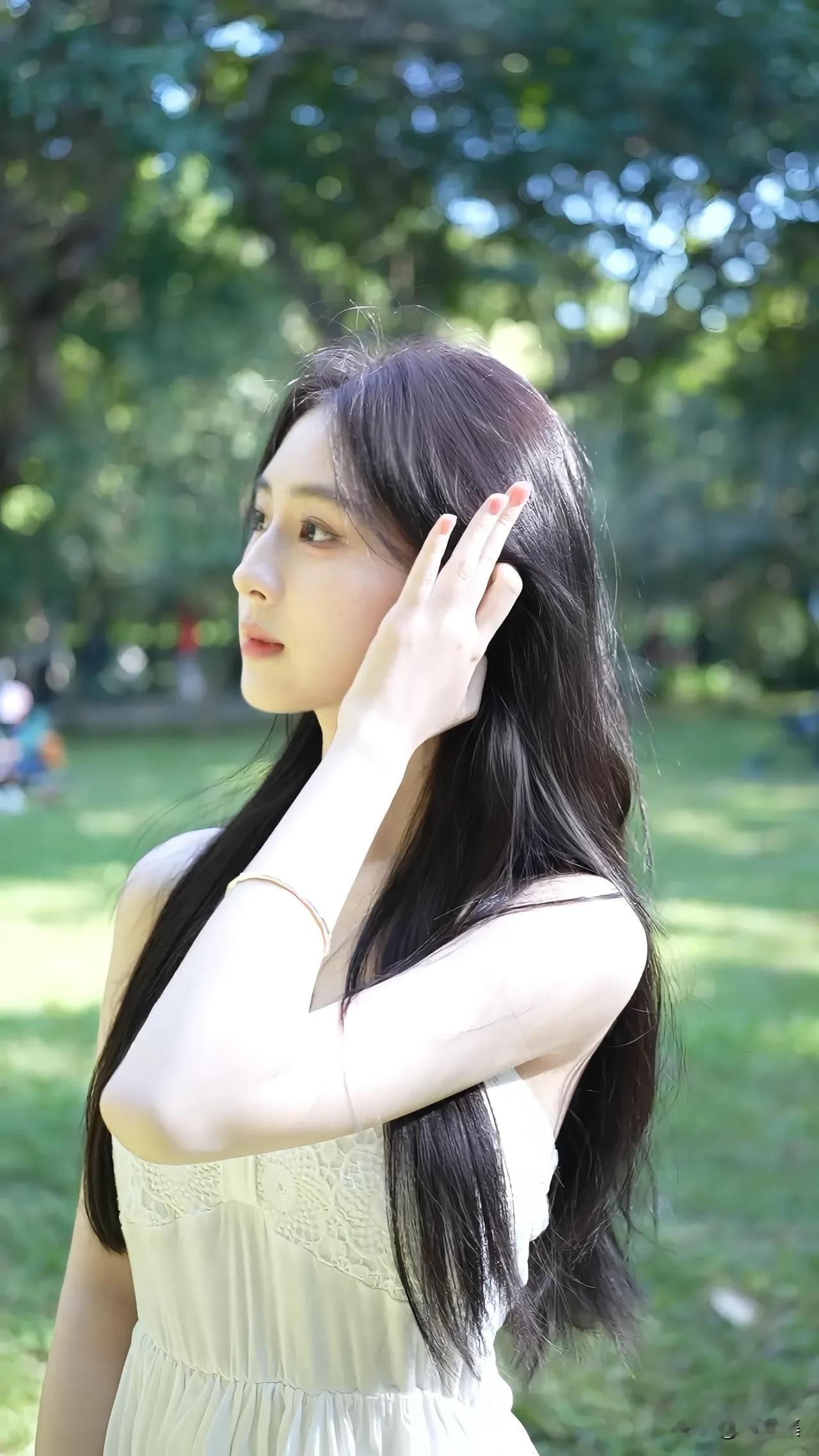 阳光洒落，少女漫步在绿意盎然的公园中，温柔地抚摸着长发，仿佛时间在这一刻静止。