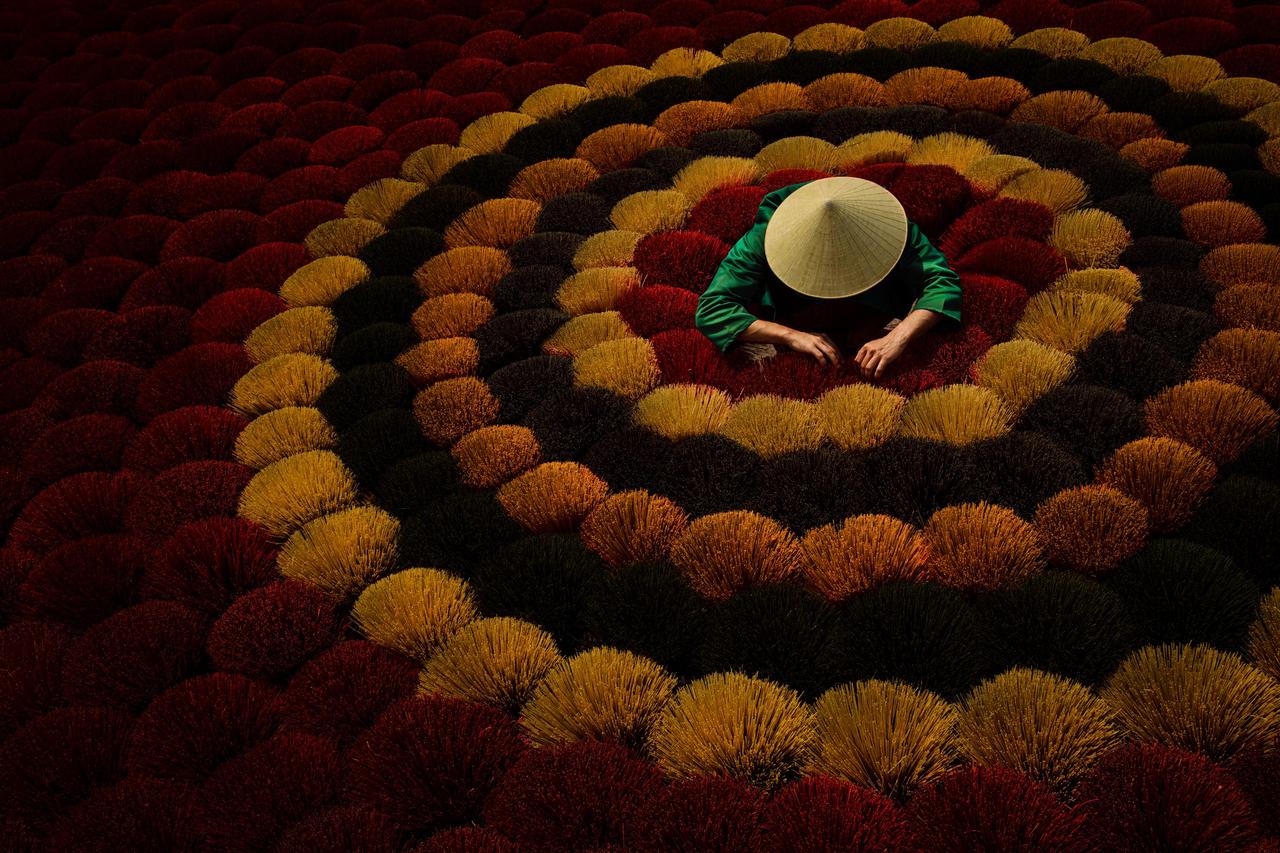 这是越南河内一个制香村晾晒香柱的场景，香柱密密麻麻铺满地面，形成鲜艳的红色海洋。