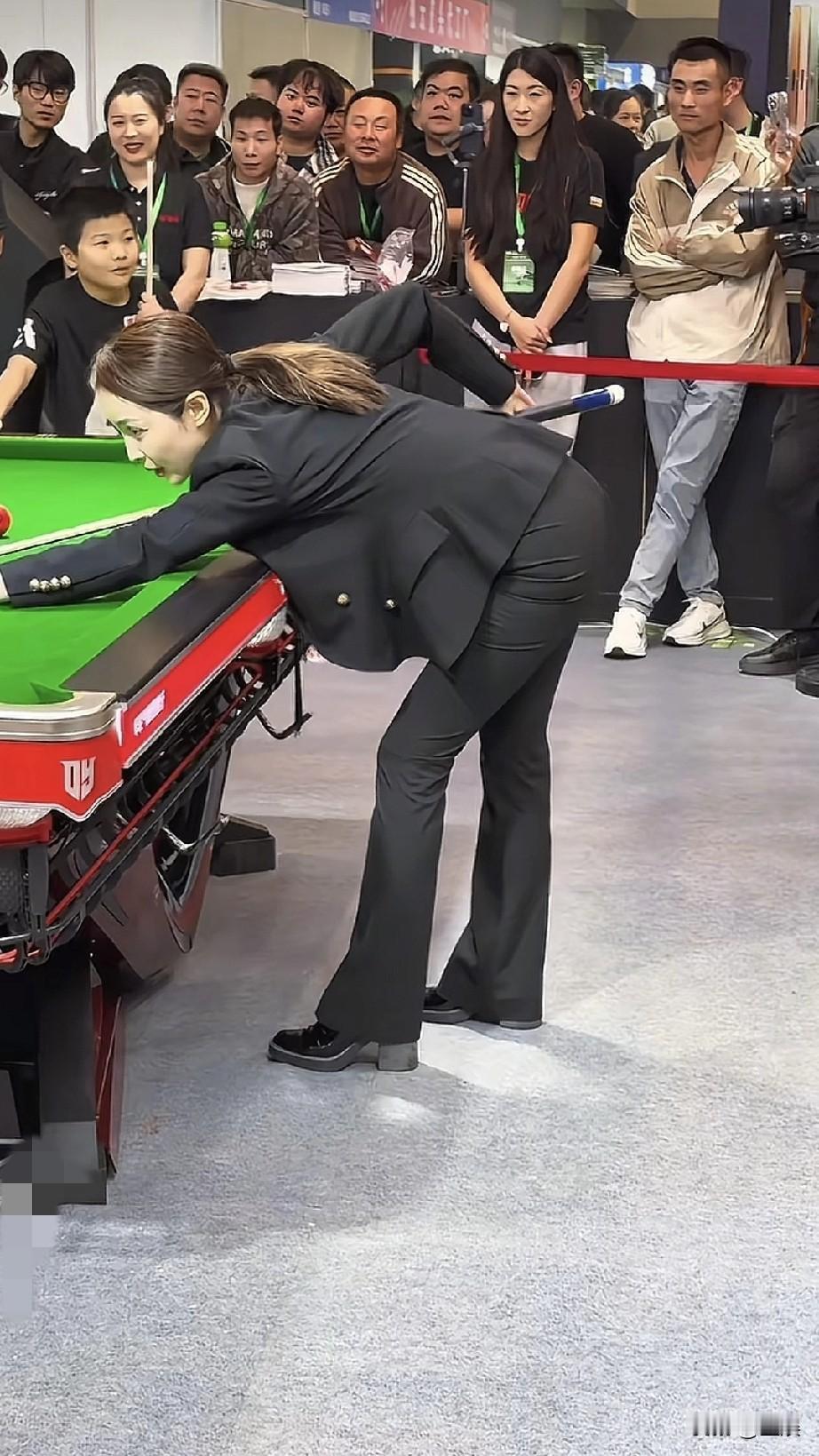 在热闹现场，王钟瑶身着干练的黑色套装，俯身专注于台球桌上的较量，专业的神情。周围