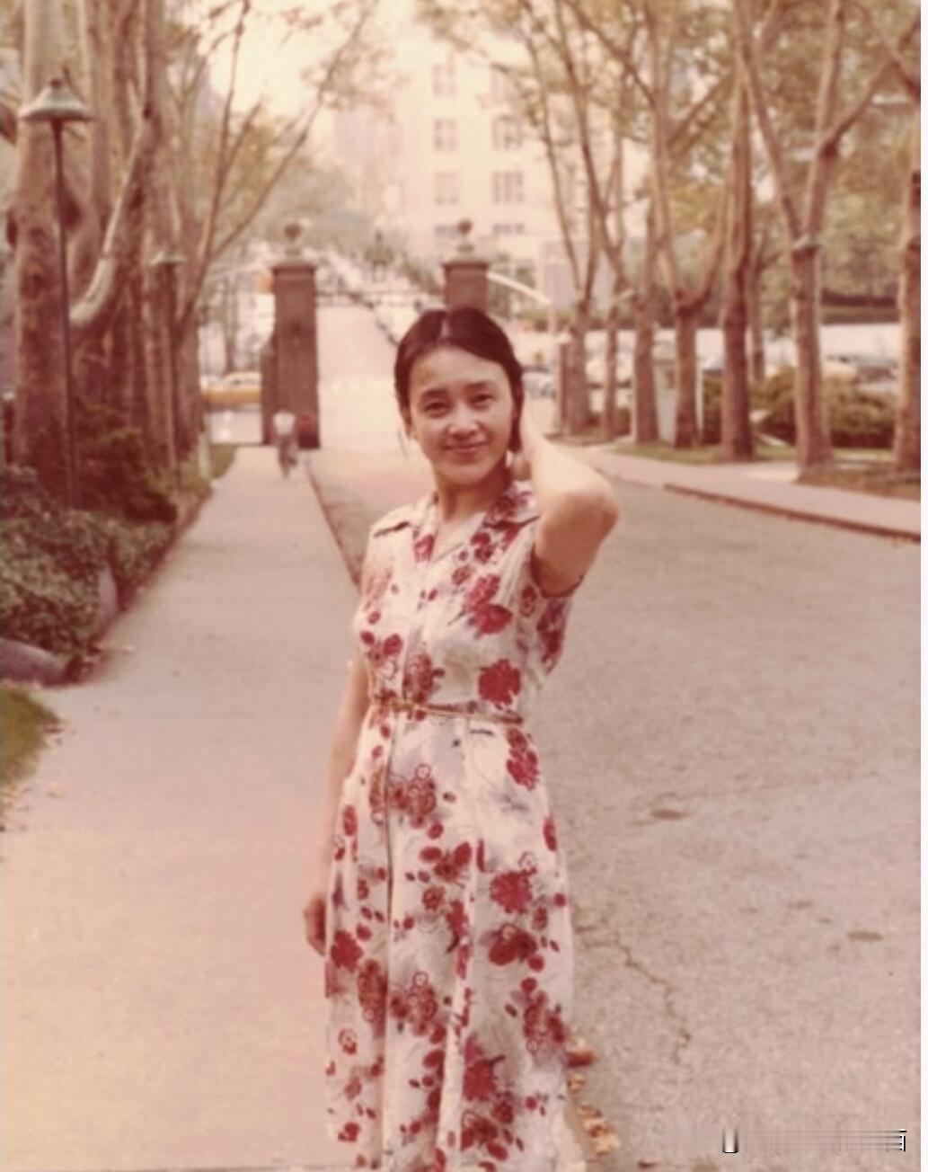 这是拍摄于80年代的老照片，她一身碎花连衣裙，优雅大方，扎着小马尾，一只手放在脖