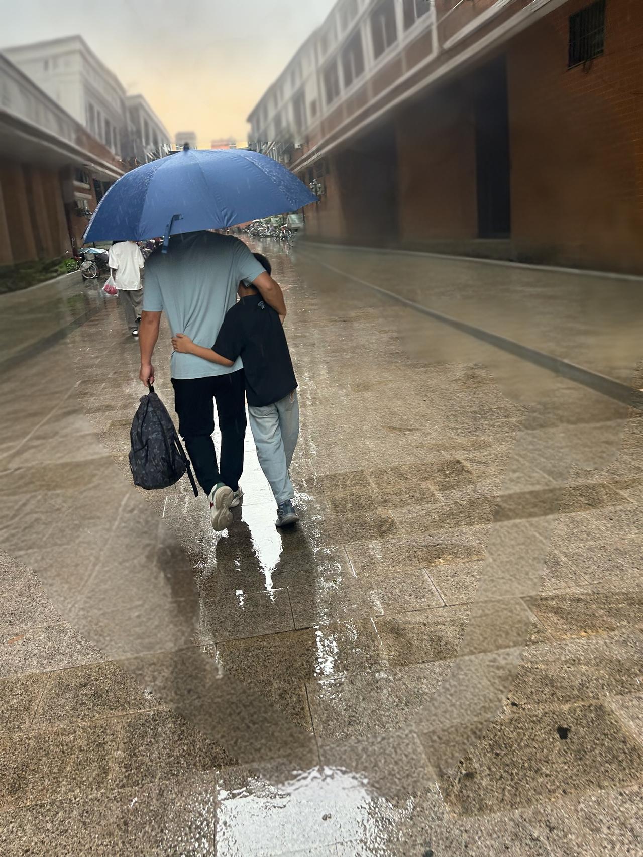 雨中送娃上学，我帮他拿书包，他帮我撑伞，妈妈在后面偷拍😄