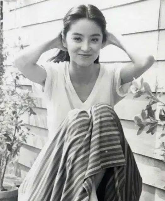 这张照片中的年轻女子她笑容甜美，气质清新，双手梳理着头发，姿态优雅，林青霞年轻时