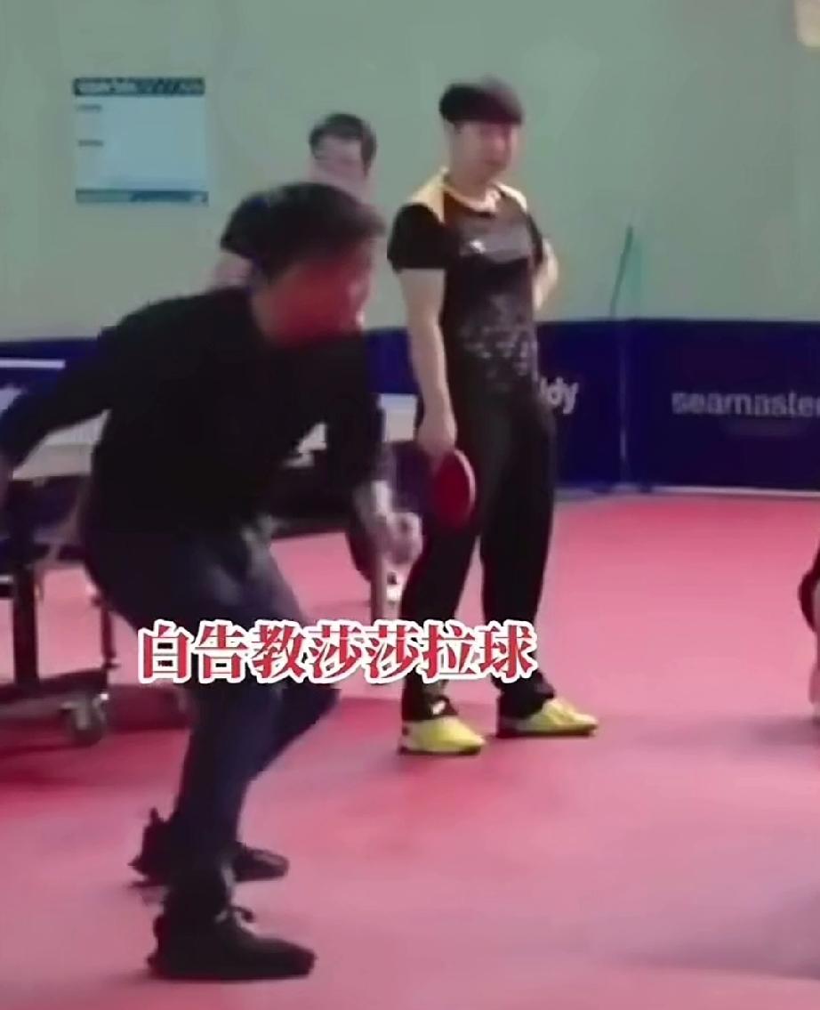 看男队主教练王皓教莎莎拉球，多认真。
莎莎拿着球拍站旁边，一手叉腰，看着王皓拉球