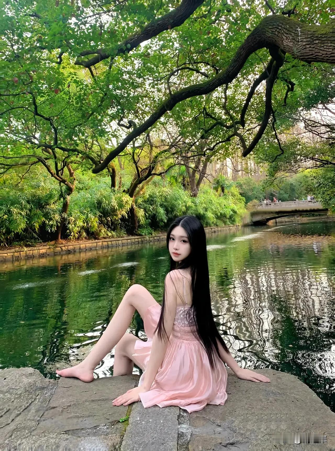 在绿意盎然的公园里，少女静坐石边，裙摆轻拂水面，宛如画中仙子。