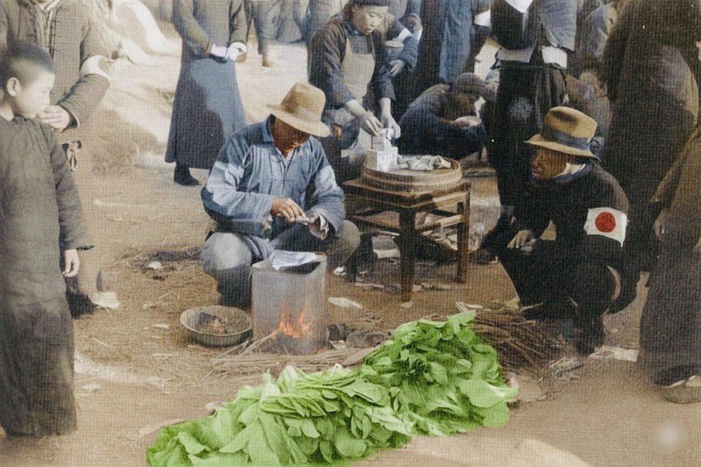 这张老照片中，地面上堆着几捆白菜、萝卜等蔬菜。两名中国男子蹲在地上，一人正在切菜