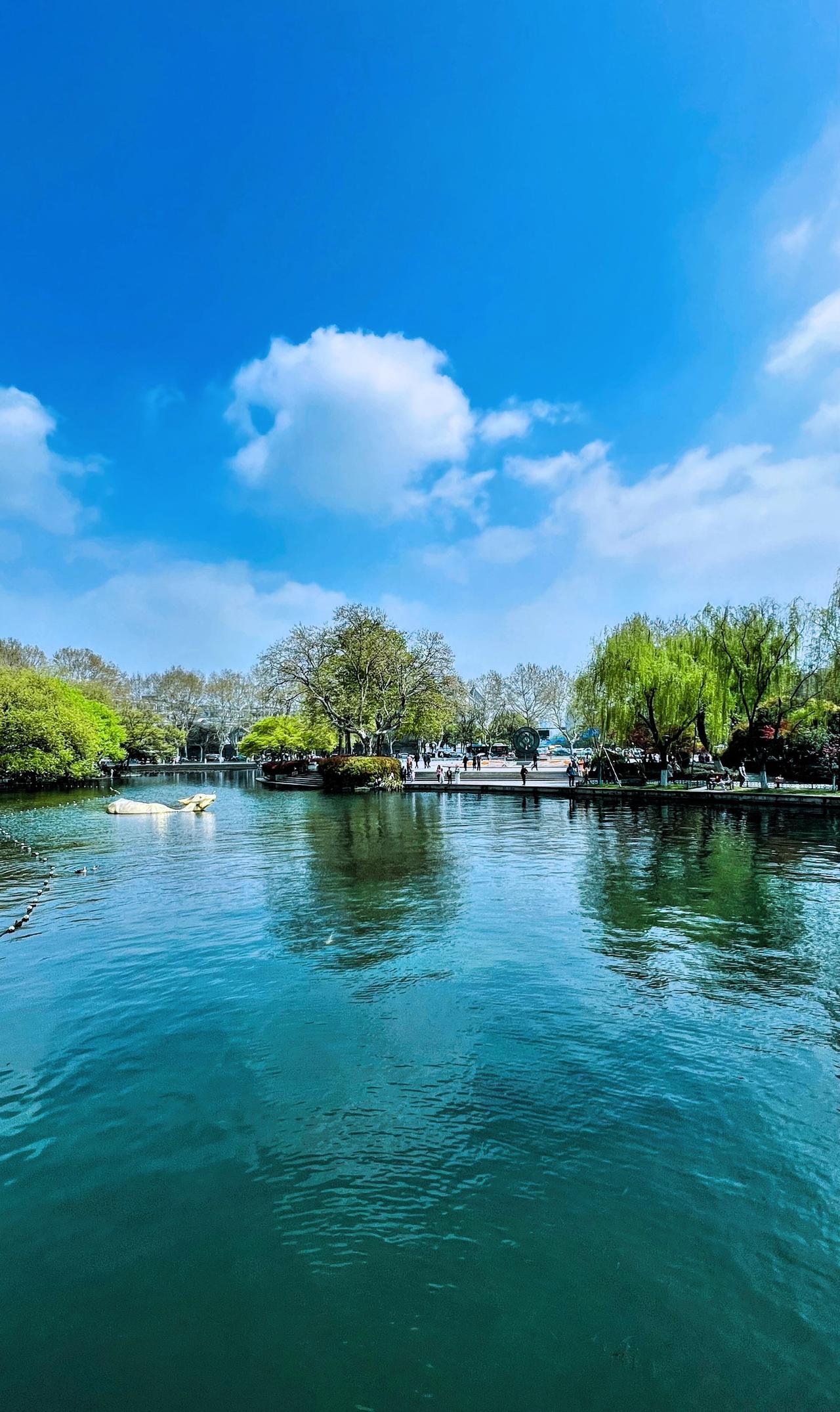 春日赏景：蓝天白云下的西湖风光：碧绿的湖水，白云悠悠，绿树环绕，美不胜收.