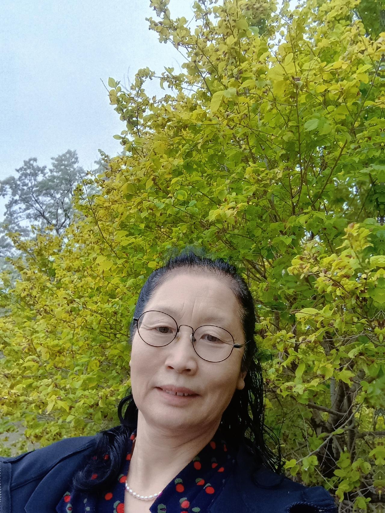 这位女士在绿树前自拍。