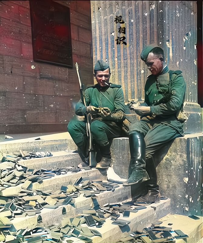 1945年，柏林解放后，两位苏联士兵坐在国会大厦前的台阶上，正在拆解他们的搜来的...