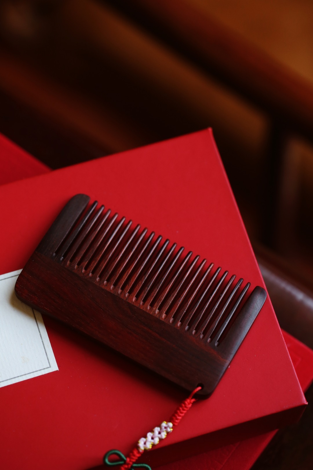 小叶紫檀【花汐】木梳百宝镶嵌之上，花儿雍容绽放；手工编织桃花结，妁妁其华；设计巧