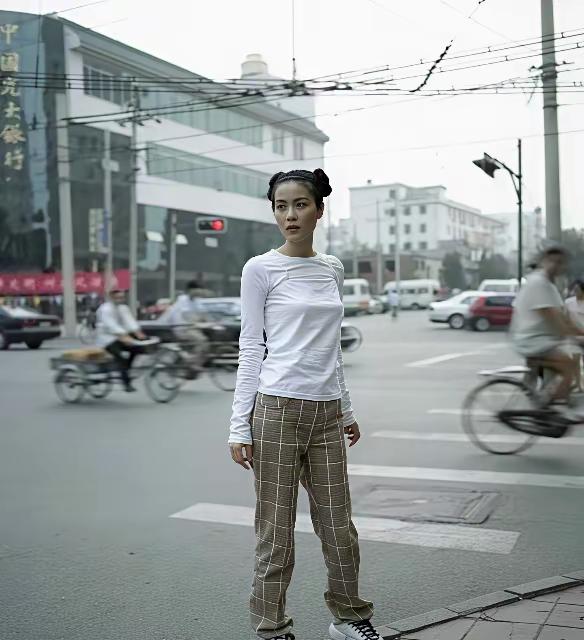 一个女孩站在街头，背景很热闹。1997年拍摄的一张照片，还认识这位大姐大吗？街头