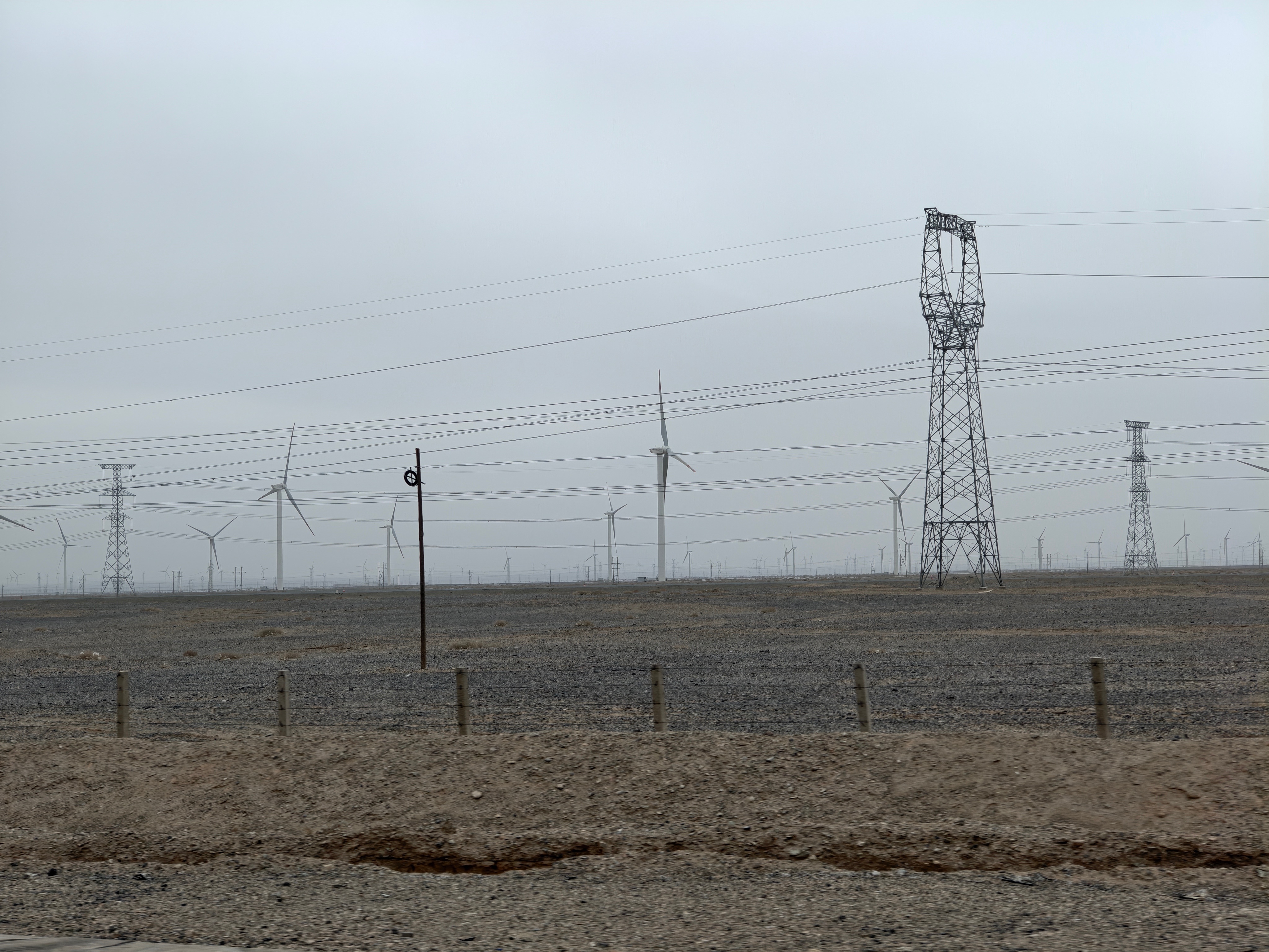 一边是密密麻麻数不清的大风车，一边是还在跋涉继续运输的风车叶片。甘肃些风力发电真