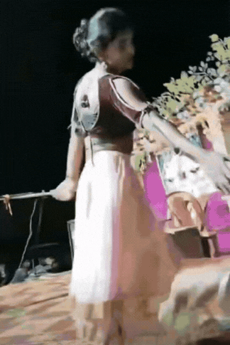 印度，一名年轻女子在舞台上跳舞，跳着跳着她看见舞台下面有人想跟她握手，为了不扫观