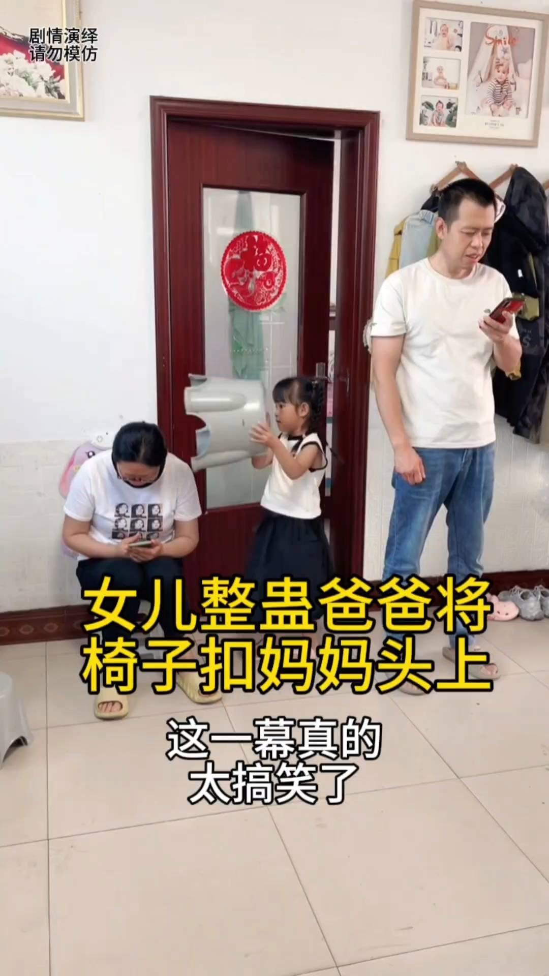 女儿整蛊爸爸将椅子扣妈妈头上。
女子坐在椅子上看手机，这时女儿看到爸爸也准备坐椅