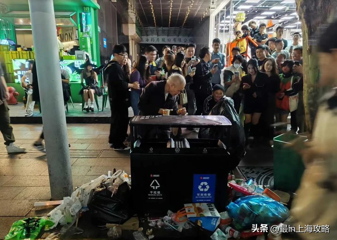上海万圣节让我感触最深的是这张图：一名流浪汉正在垃圾桶里捡吃的，旁边是一群人在拍