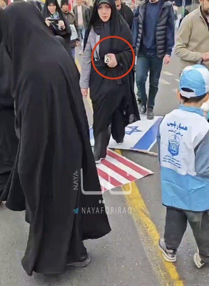 这又是来自伊朗的黑色幽默，一个黑袍女嚣张的踩着美国和以色列国旗，但是手上拿的是I