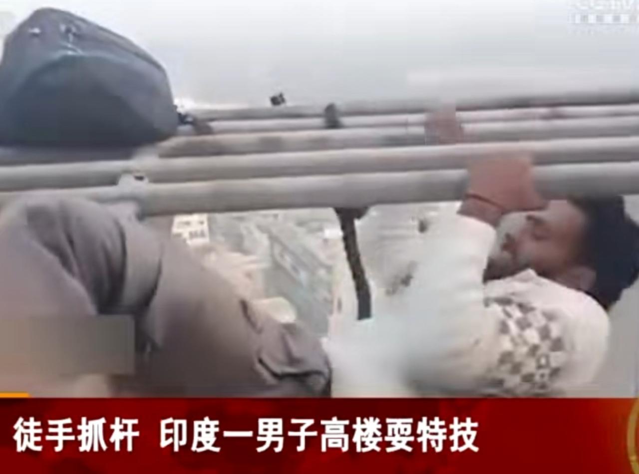 在印度的高空之上，一名男子正上演着惊险一幕。他徒手抓着高楼外的金属杆，身体悬空在