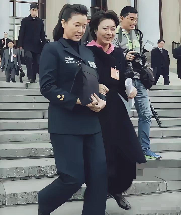 宋祖英李胜素挽着胳膊一起走下台阶。
宋祖英一身深色西服，端庄大气；李胜素黑色长款