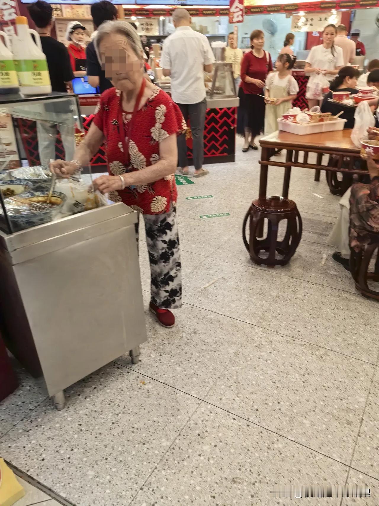今天中午去蔡林记吃饭，无意间看到这位80多岁的老婆婆正拿着一个朔料袋子，把桌上的