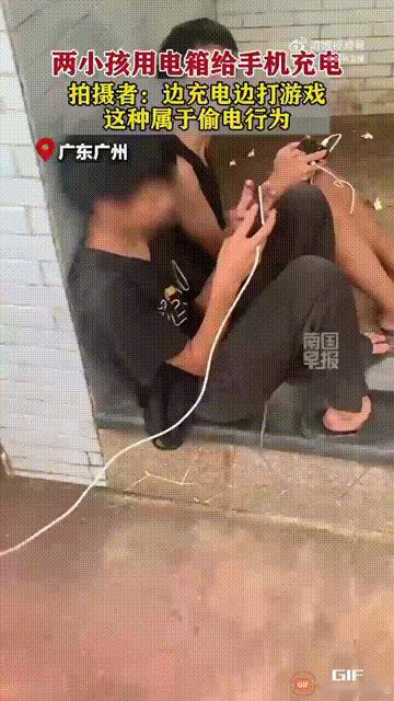广东广州两个只有十几岁的孩子，在街头使用公共电箱为手机充电，而他们则拿着手机打游