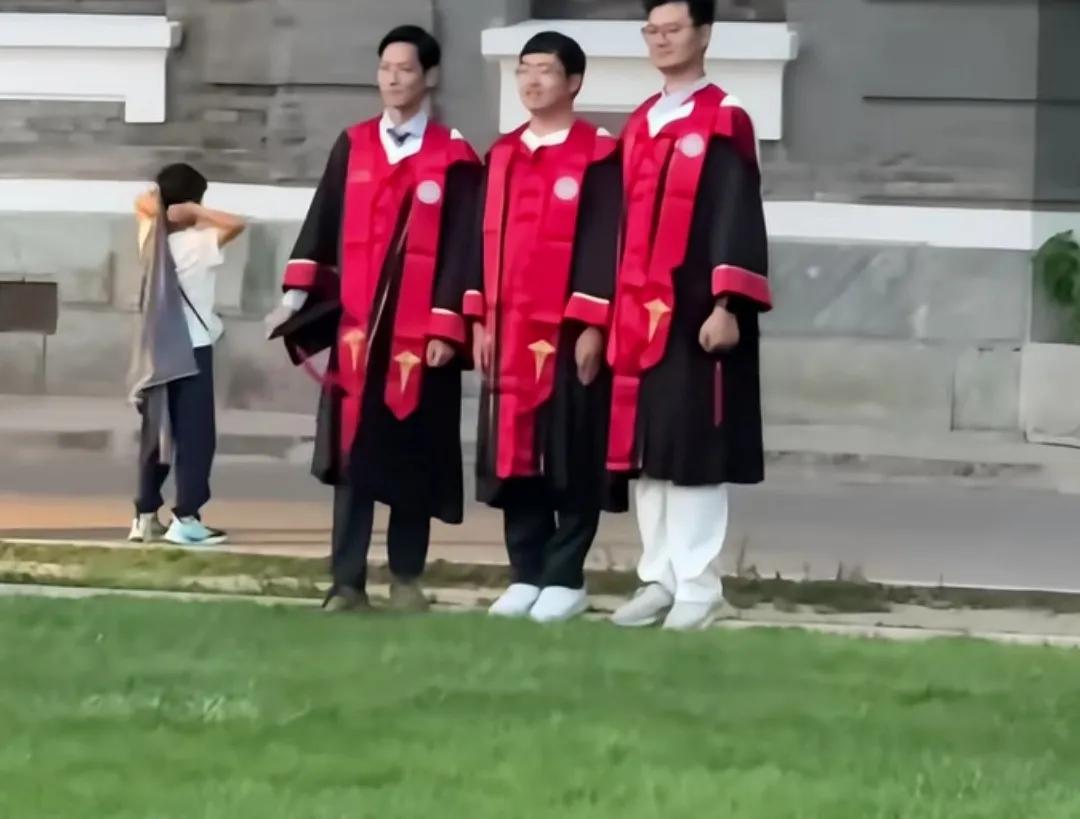 三位男生身穿红色毕业战袍合影。