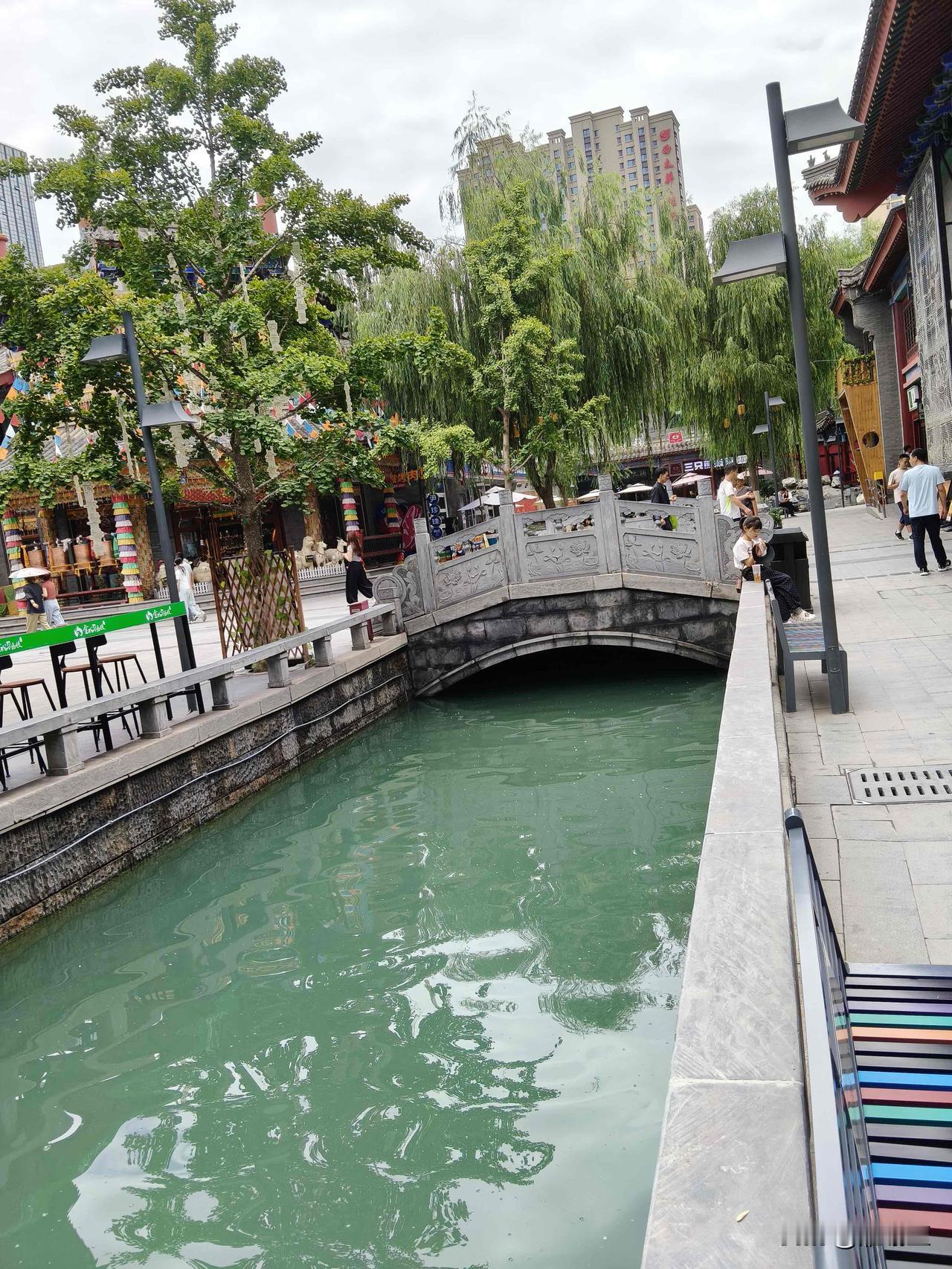 雨过天晴逛兰州老街，河道中段一座古朴石拱桥横跨水面，桥身连接街巷深处，远处高楼隐