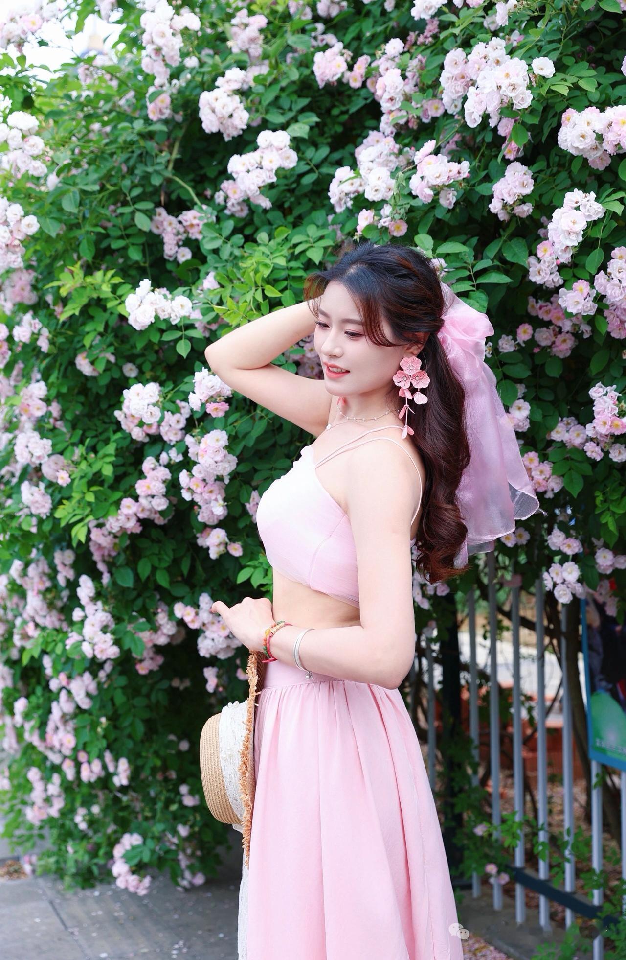 记录我的2026背靠花海之中的甜美少女，轻抚黑发，一身粉裙与粉花相映成趣。