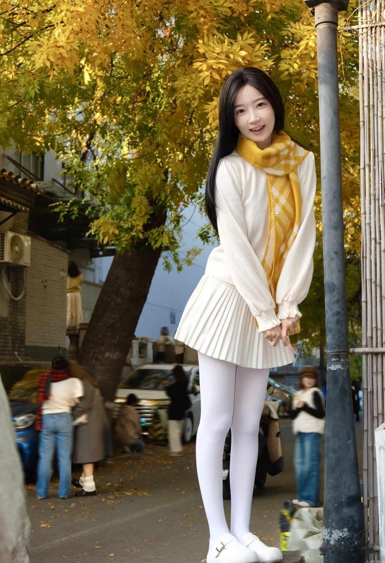 秋天街角，女孩靠在灯柱旁微笑。